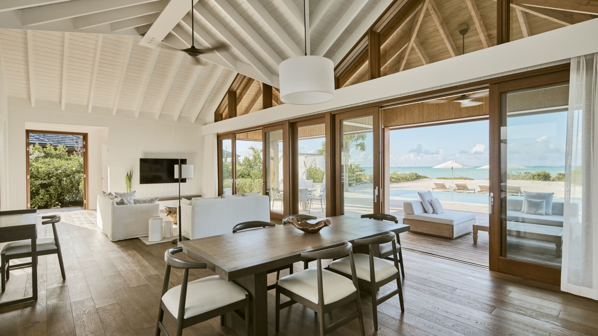 A light-filled interior with exposed roof beams and timber-framed doors opening towards the sea